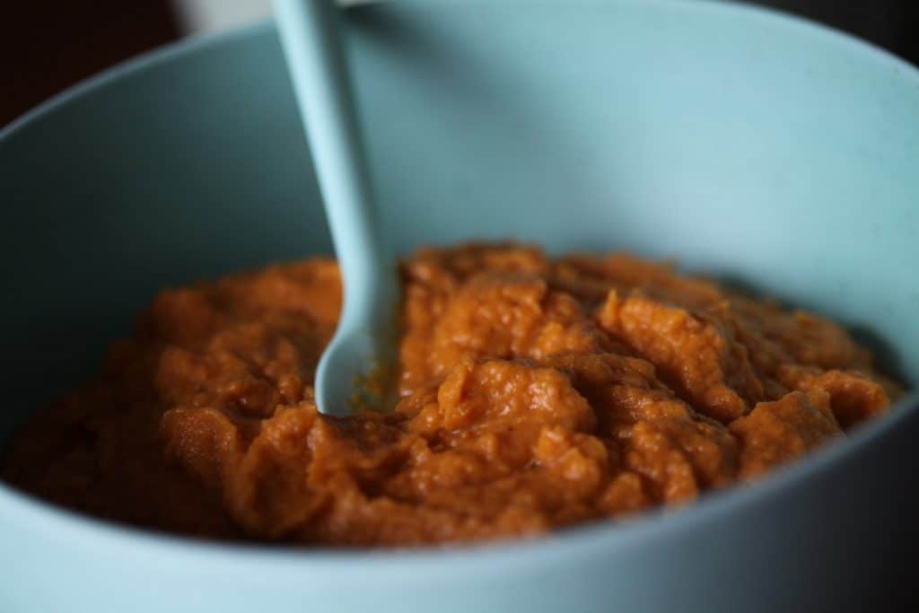 cooked sweet potatoes in a blue bowl with a blue spoon