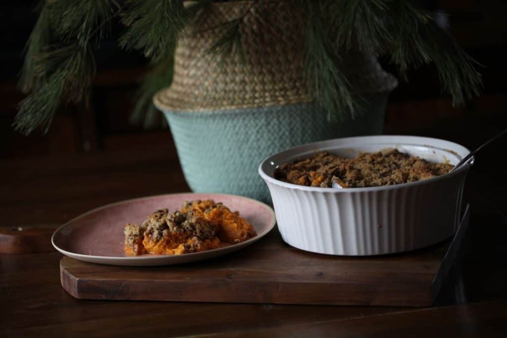 casserole cooked and served, sitting on a brown cutting board next to a basket with pine boughs