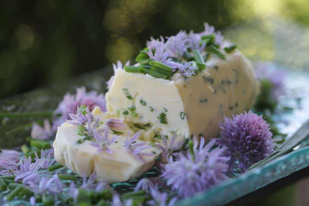 chive butter on a glass plate, garnished with bits of chive and chive blossoms, showing how to use fresh chives from the garden