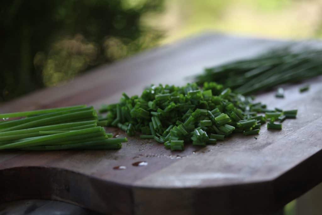 wooden cutting board with chives chopped, showing how to use fresh chives from the garden