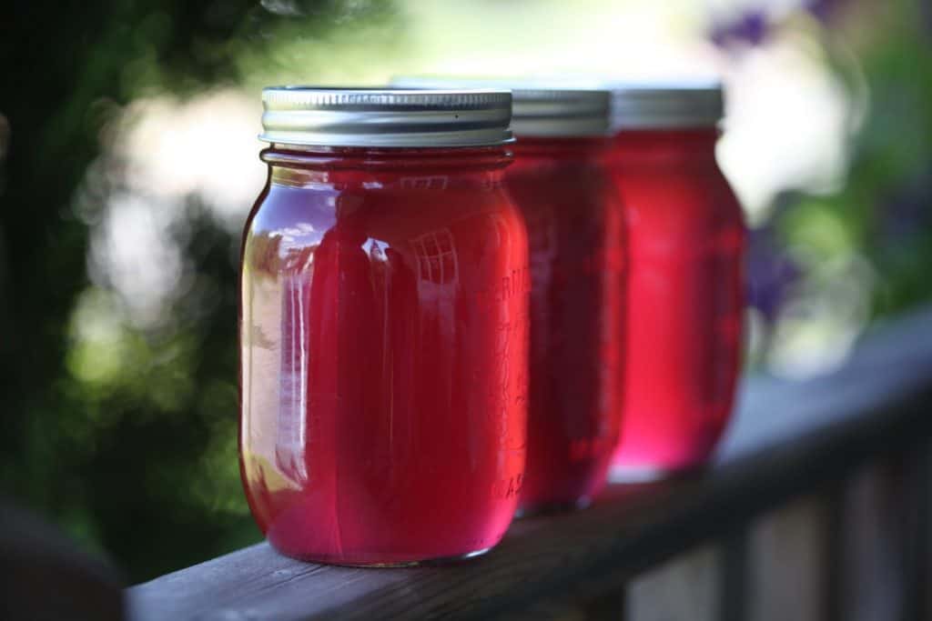 three mason jars filled with pink jelly on a railing