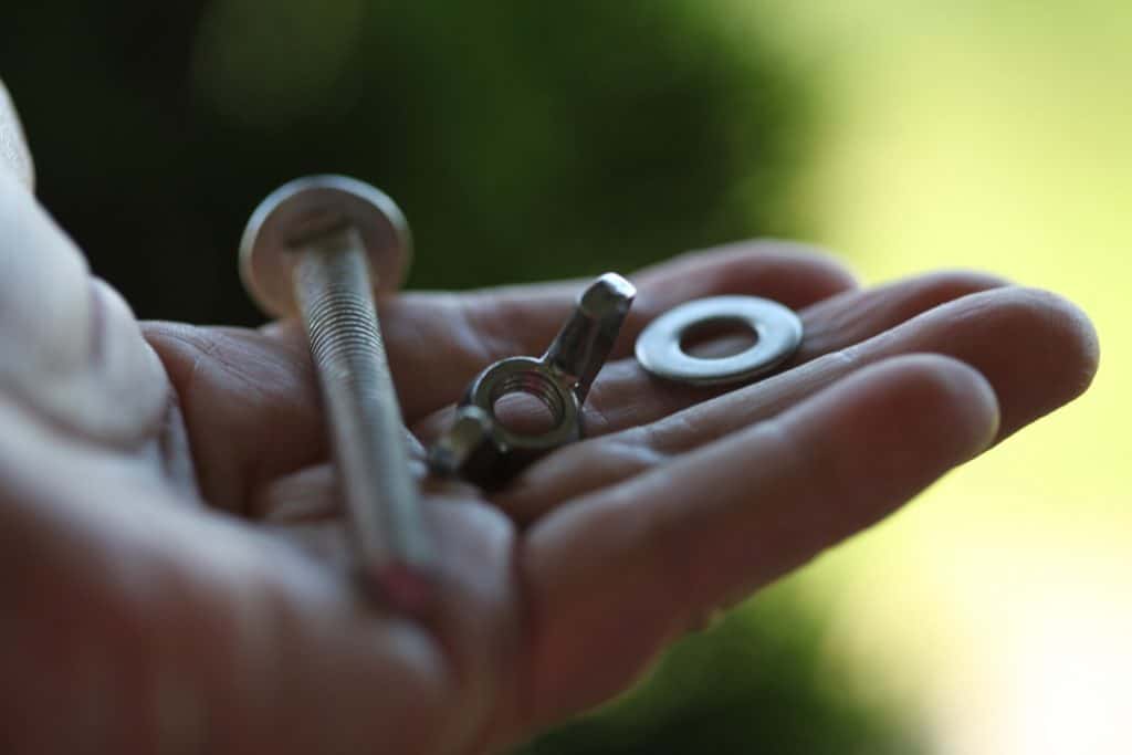 a hand holding a bolt, wing nut and washer