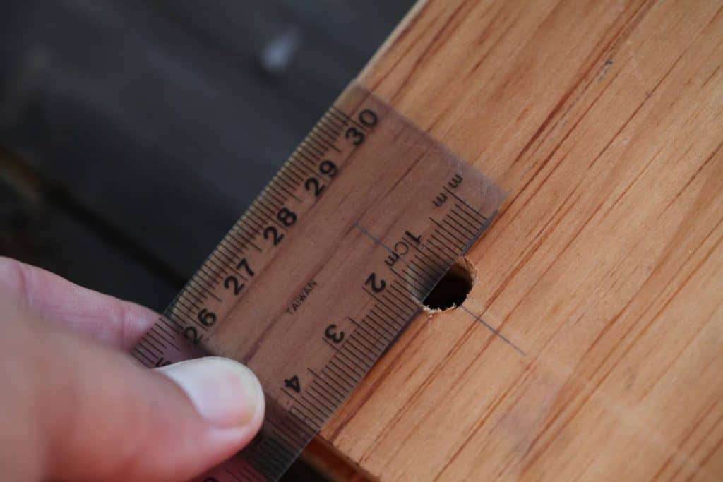 a hand holding a ruler against a piece of wood