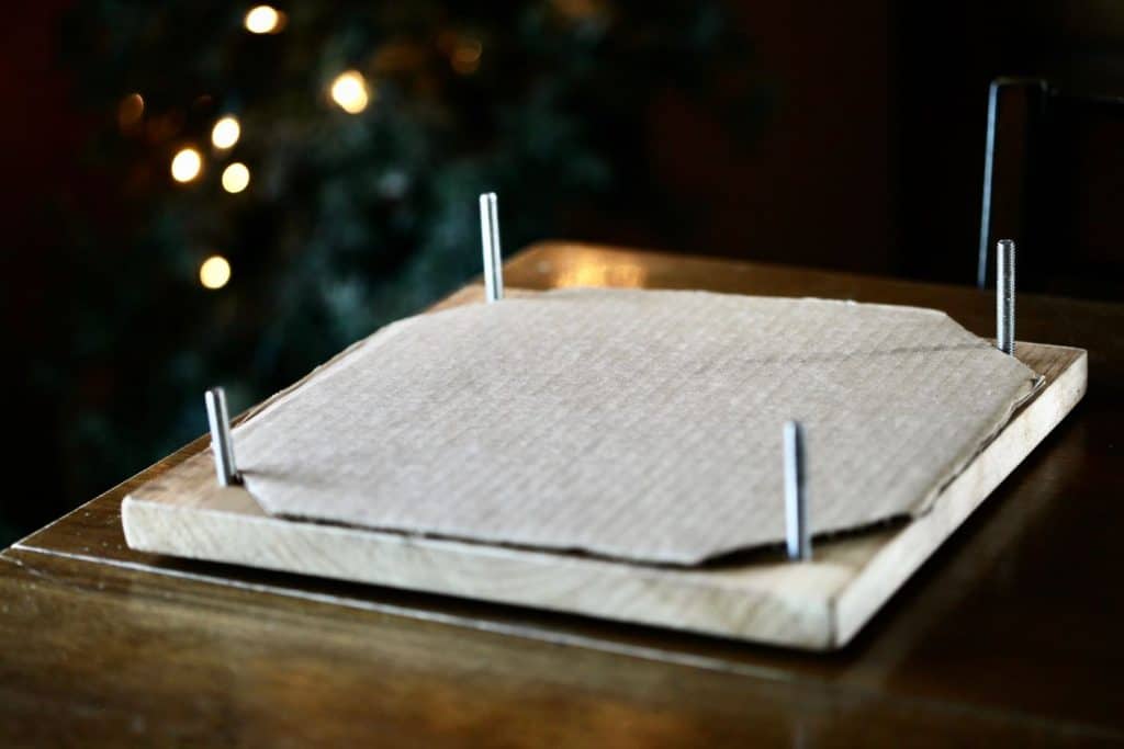 cardboard placed on a wooden flower press with white mini lights in the background