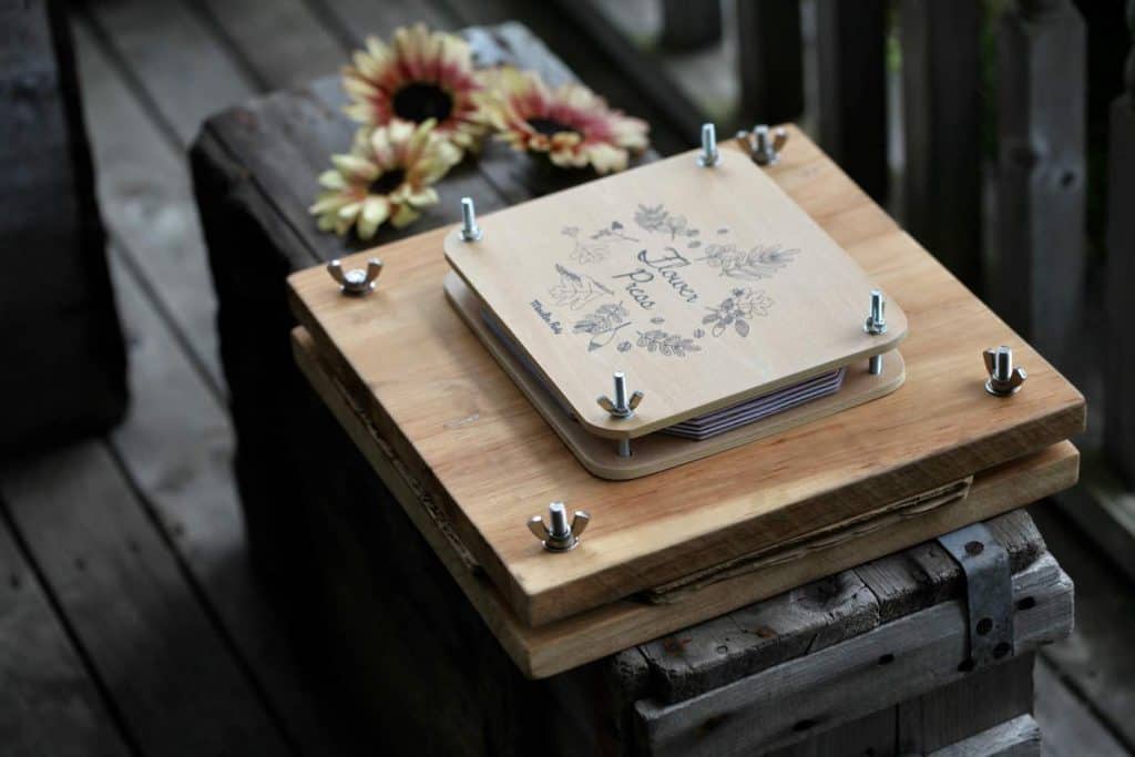 two flower presses of different size, on a grey wooden crate with sunflowers in the background