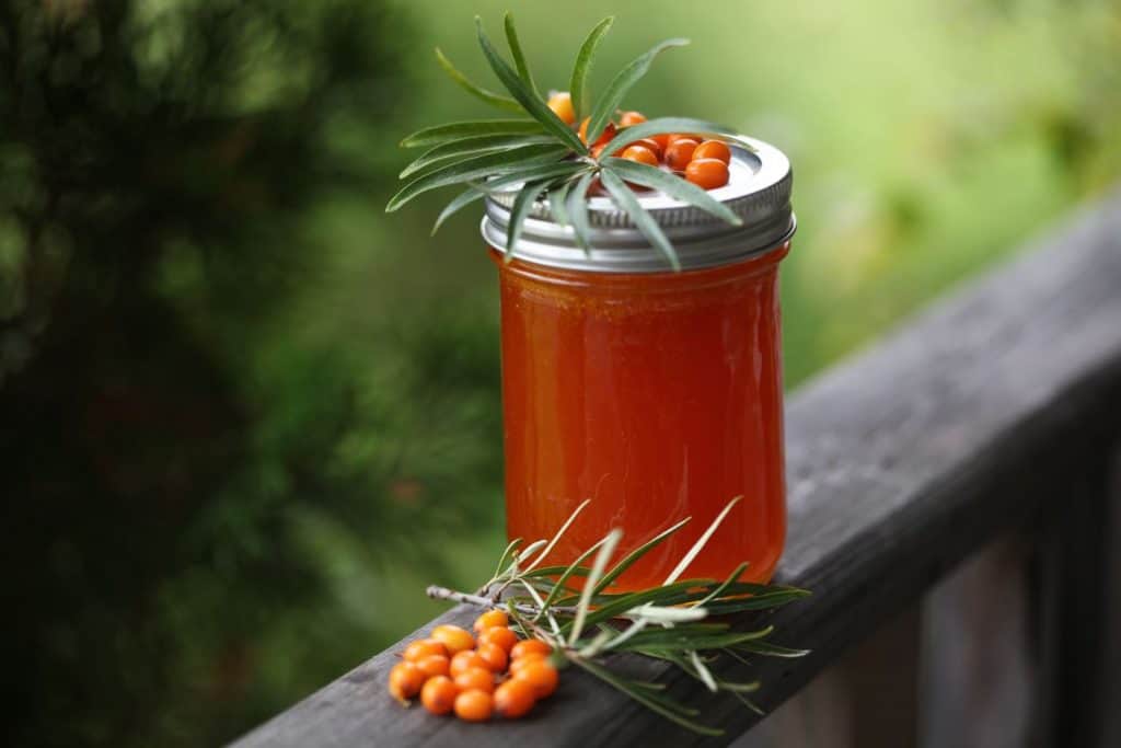 a jar of orange sea buckthorn jam, decorated with leaves and orange berries, on a wooden railing