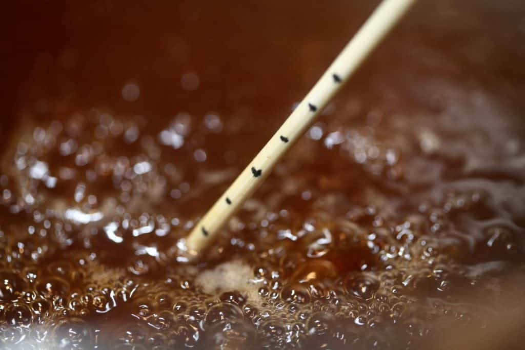 a pot of boiling apple cider with a wooden skewer inserted to gauge the depth of the cider