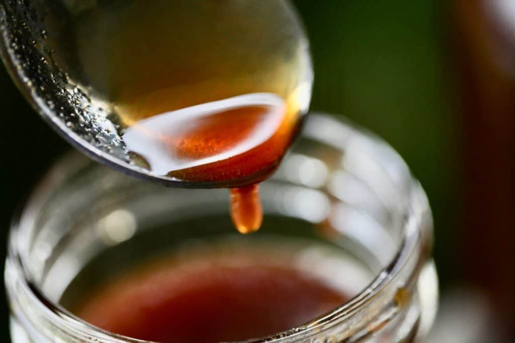 a spoon over a jar of apple cider syrup, showing the perfect consistency of the syrup by dripping some into the container