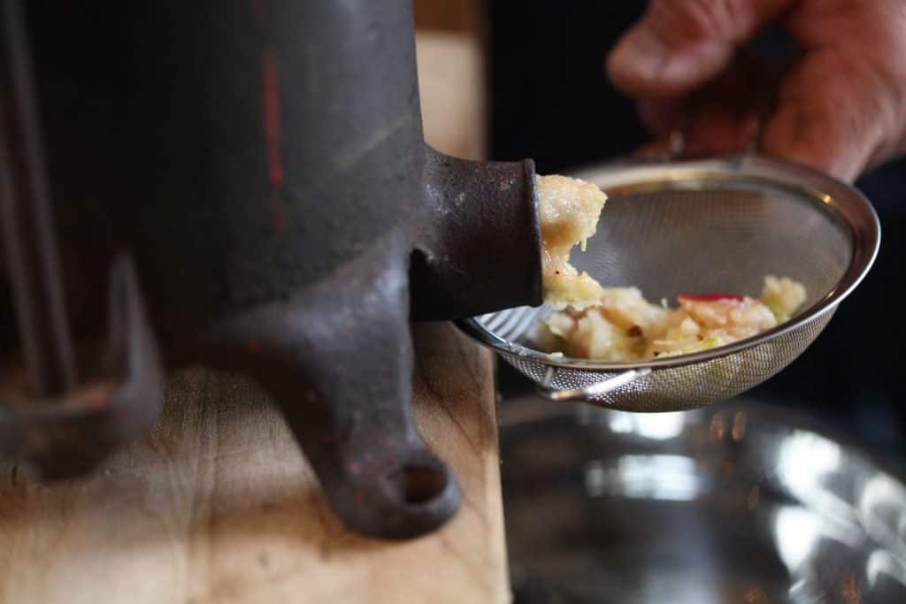 a hand holding a sieve catching the apple mash from an apple press