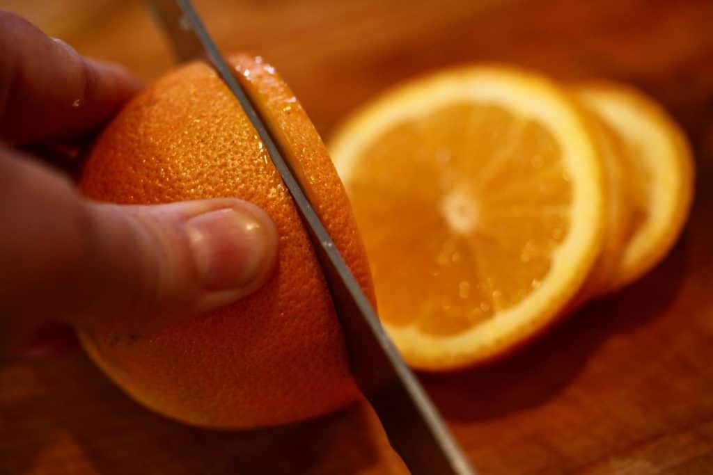 a hand holding an orange and cutting slices