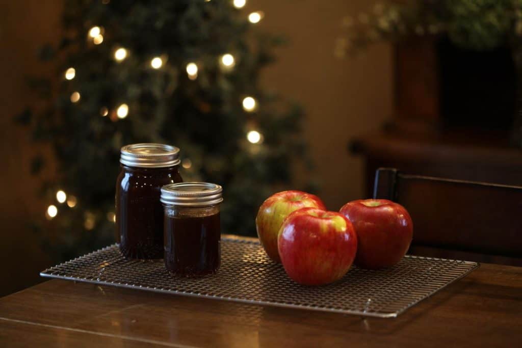 two mason jars full of fresh apple cider syrup cooling on a rack next to three red apples