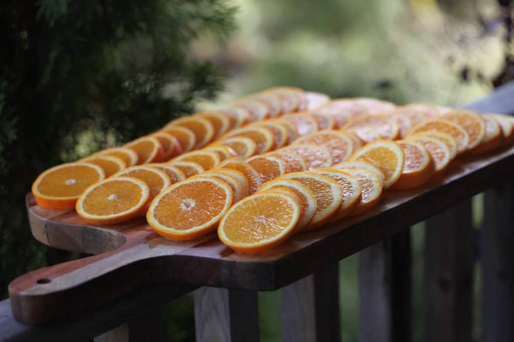 dried orange slices freshly prepared for drying, arranged in rows on a wooden cutting board