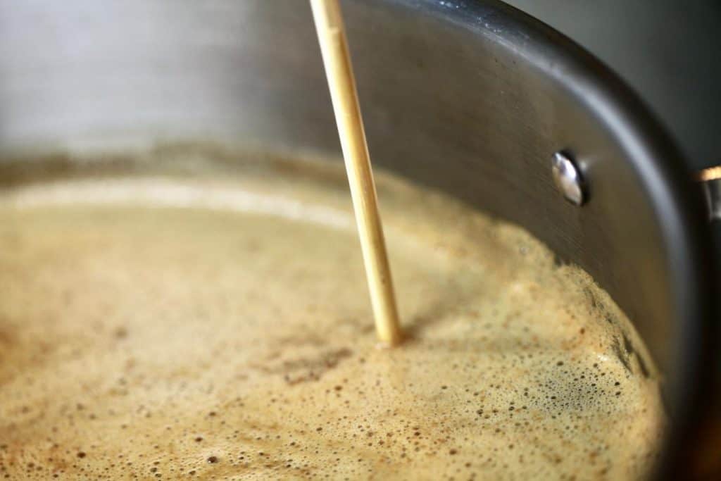 a pot of boiling apple cider with a wooden skewer inserted to gauge the depth of the cider