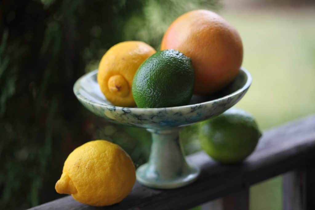 an alabaster platter with lemons, limes and grapefruit, on a wooden railing