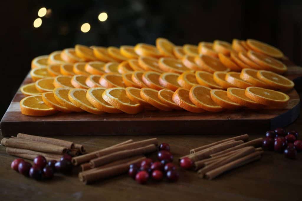 prepared orange slices ready to be dried, on a wooden cutting board in front of cinnamon sicks and cranberries