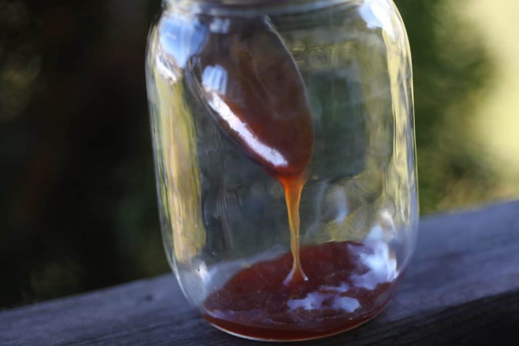 a mason jar with apple cider syrup and a spoon, showing how to reconstitute the syrup