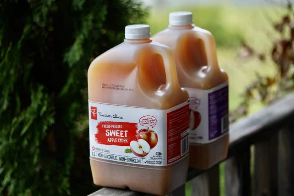 two jugs of store bought apple cider on a wooden railing