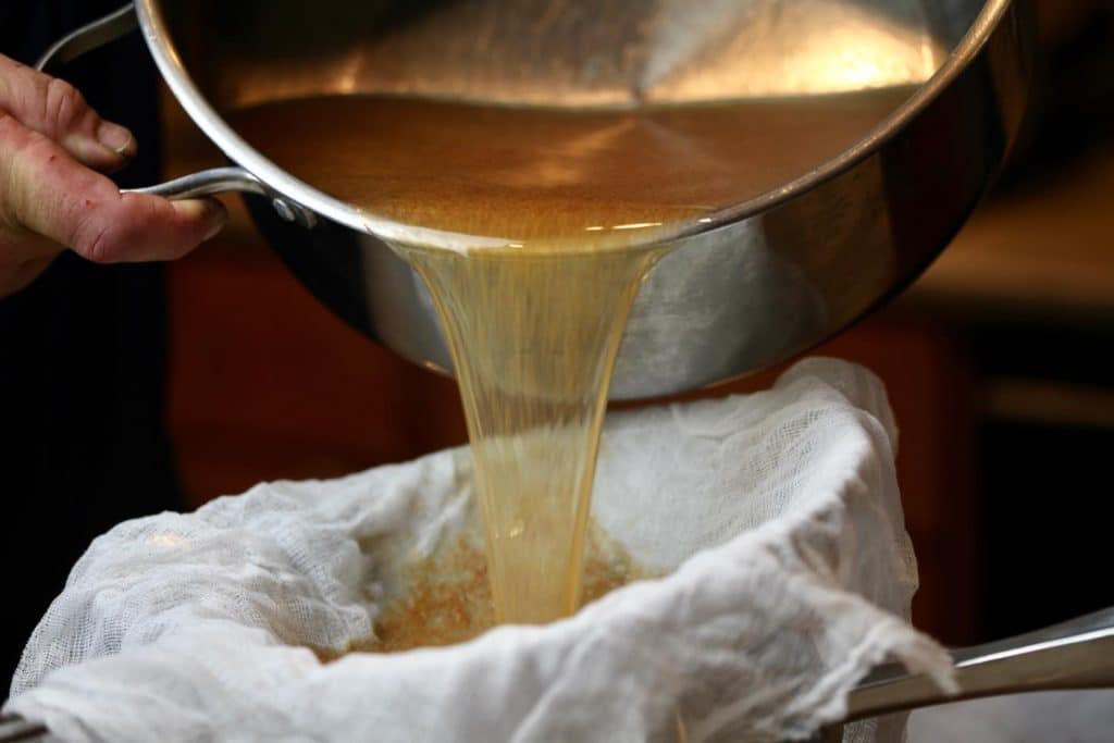straining apple cider by pouring into  a cheesecloth covered fine mesh strainer
