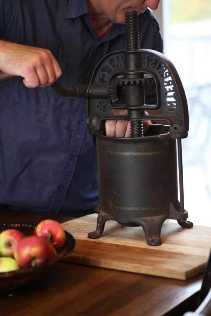 a man turning the handle of the apple press compressing the apple pieces inside