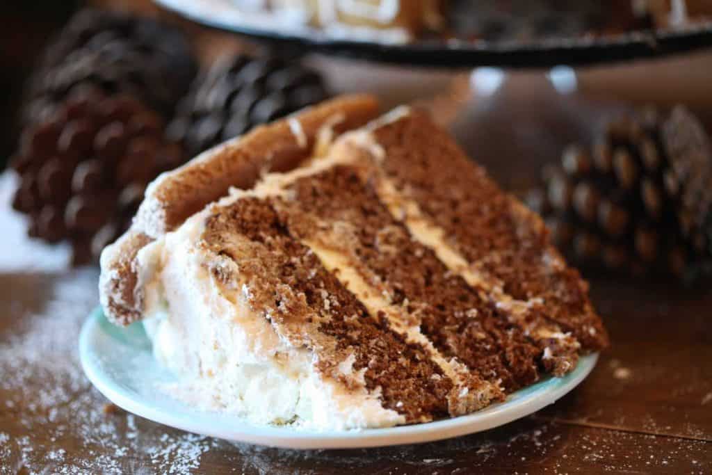 a slice of gingerbread cake with cream cheese frosting on a small plate, surrounded by pinecones