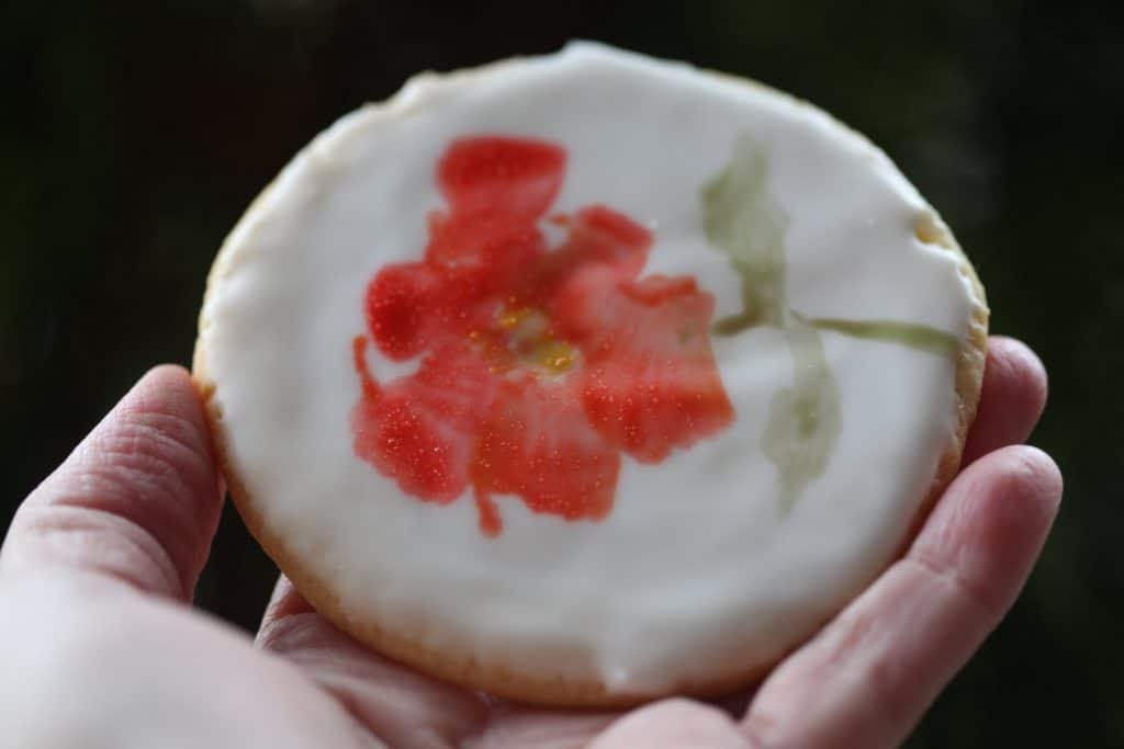 a hand holding a cookie showing a flower painted with edible watercolor on a sugar cookie