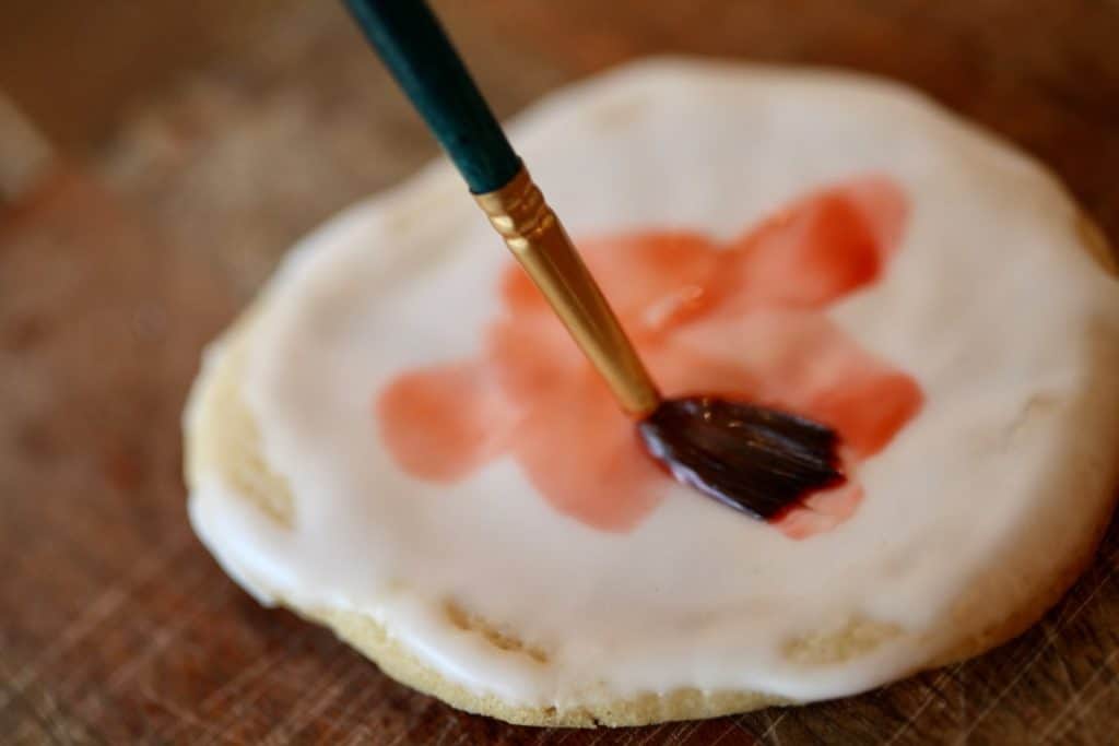 a paintbrush painting a flower on a cookie