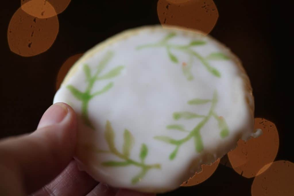a hand holding a cookie showing leaves painted with edible watercolor on a sugar cookie
