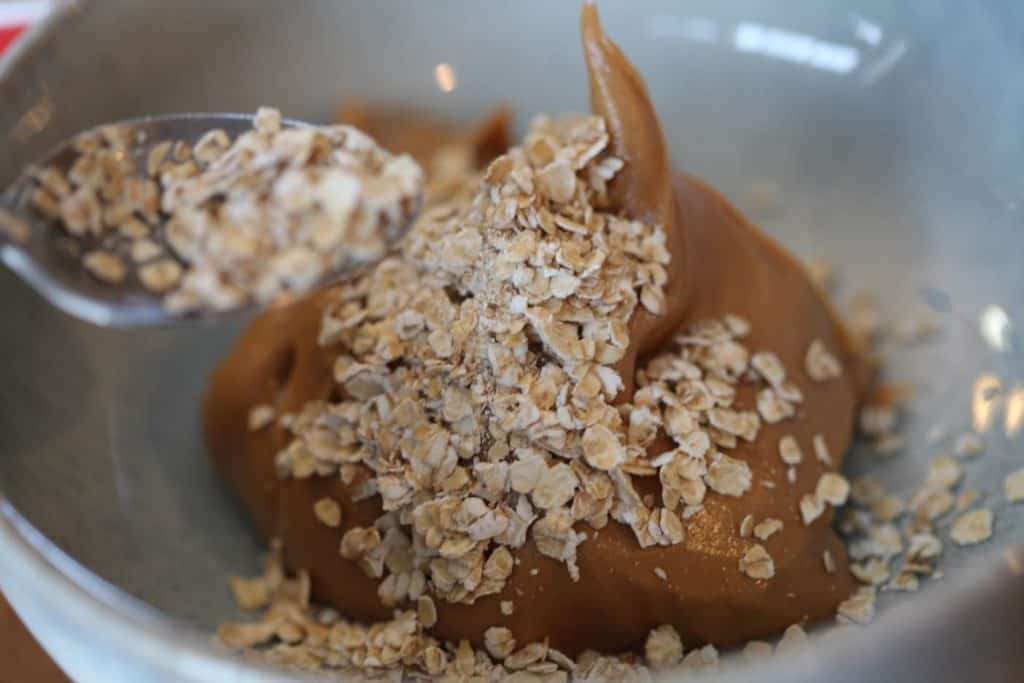 peanut butter and rolled oats in a blue bowl with a spoon of rolled oats above the bowl