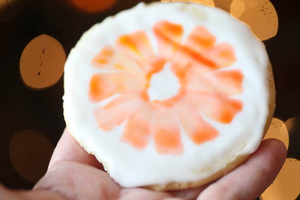 a hand holding a cookie showing an orange slice painted with edible watercolor on a sugar cookie