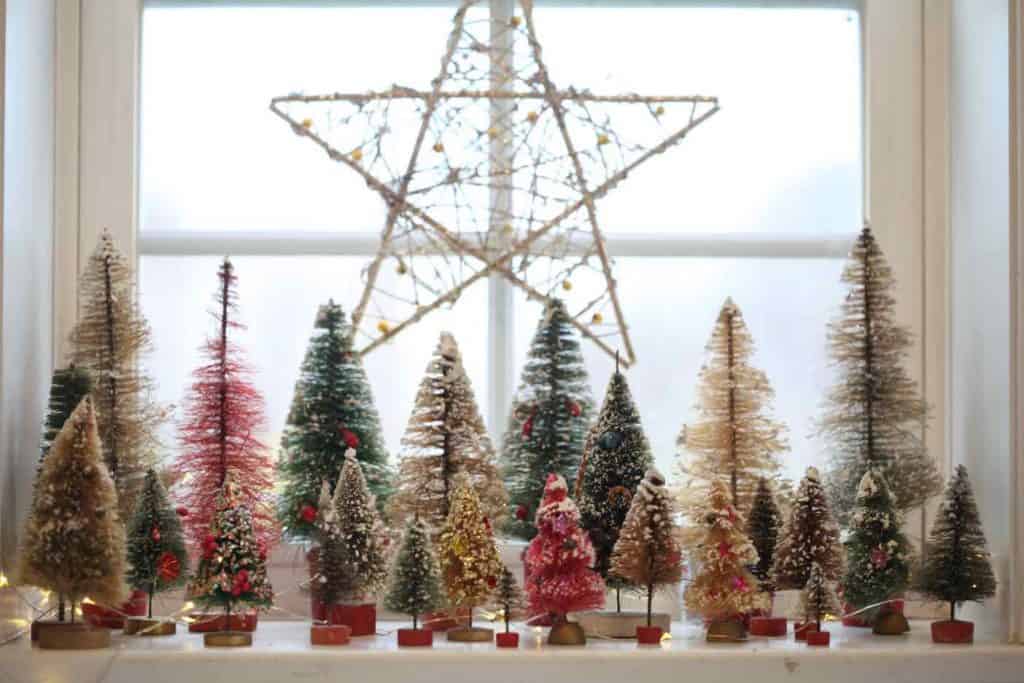 a display of vintage bottle brush trees   in many sizes, shapes and colours on a window sill