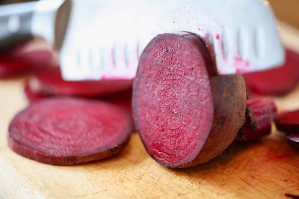 a knife slicing a beet into thin slices on a wooden cutting board