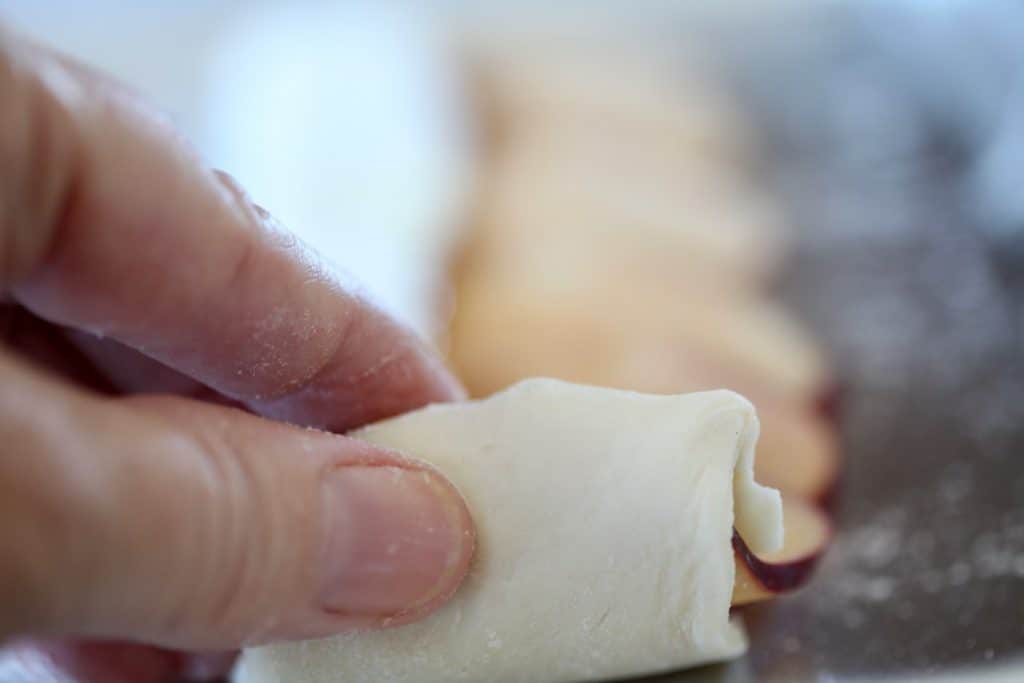 a hand carefully rolling the pastry and apple slices together from one end of the pastry