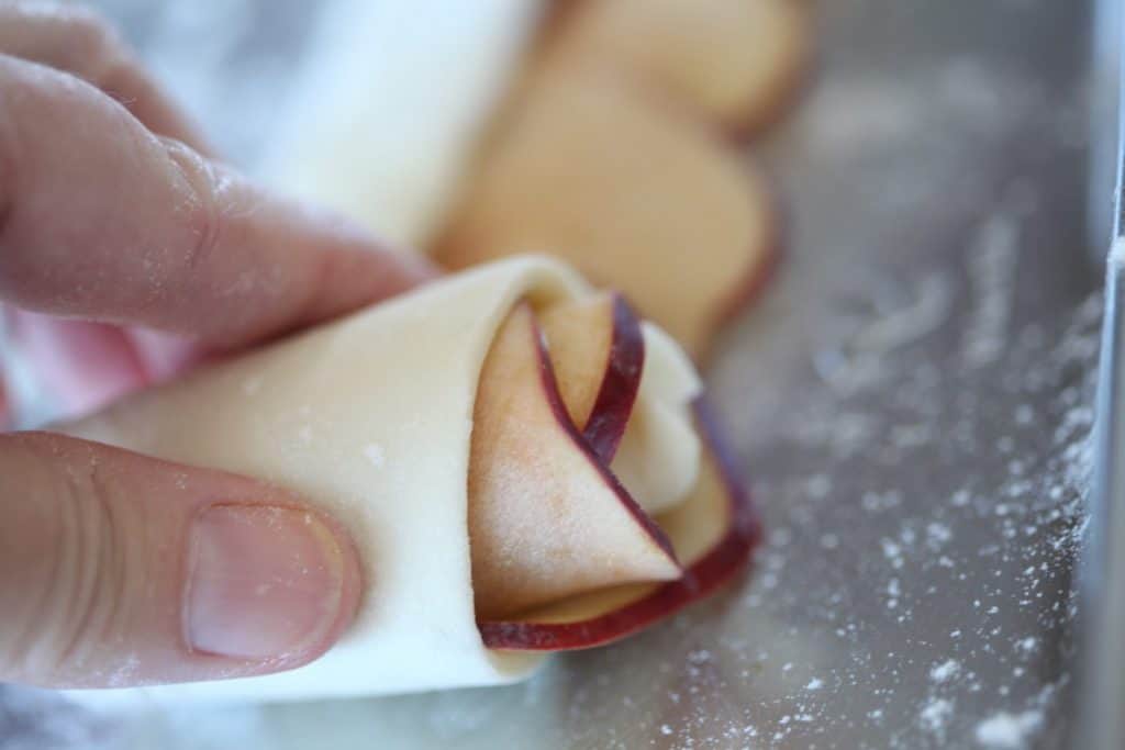 a hand rolling apple roses in puff pastry