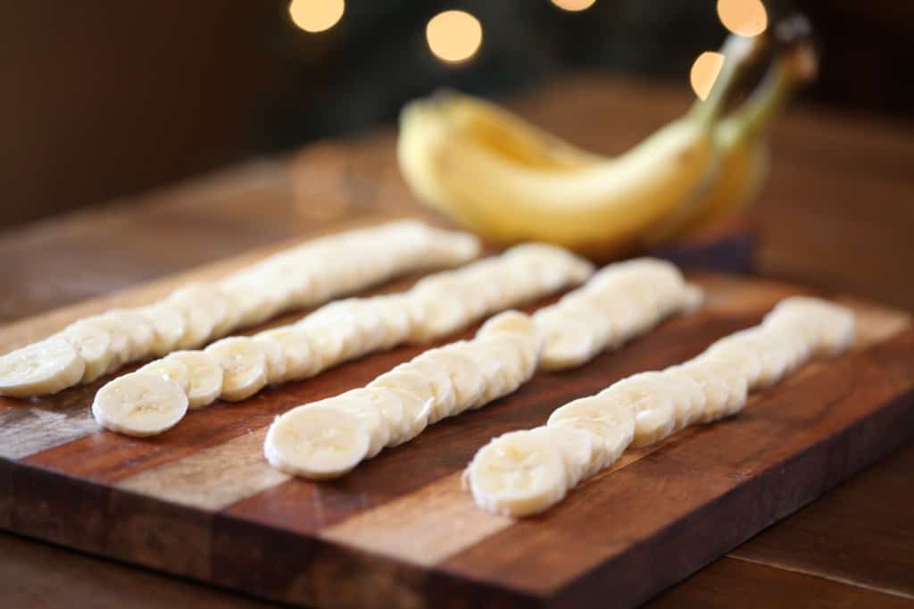 slices of bananas on a wooden cutting board, ready to be dehydrated in the air fryer