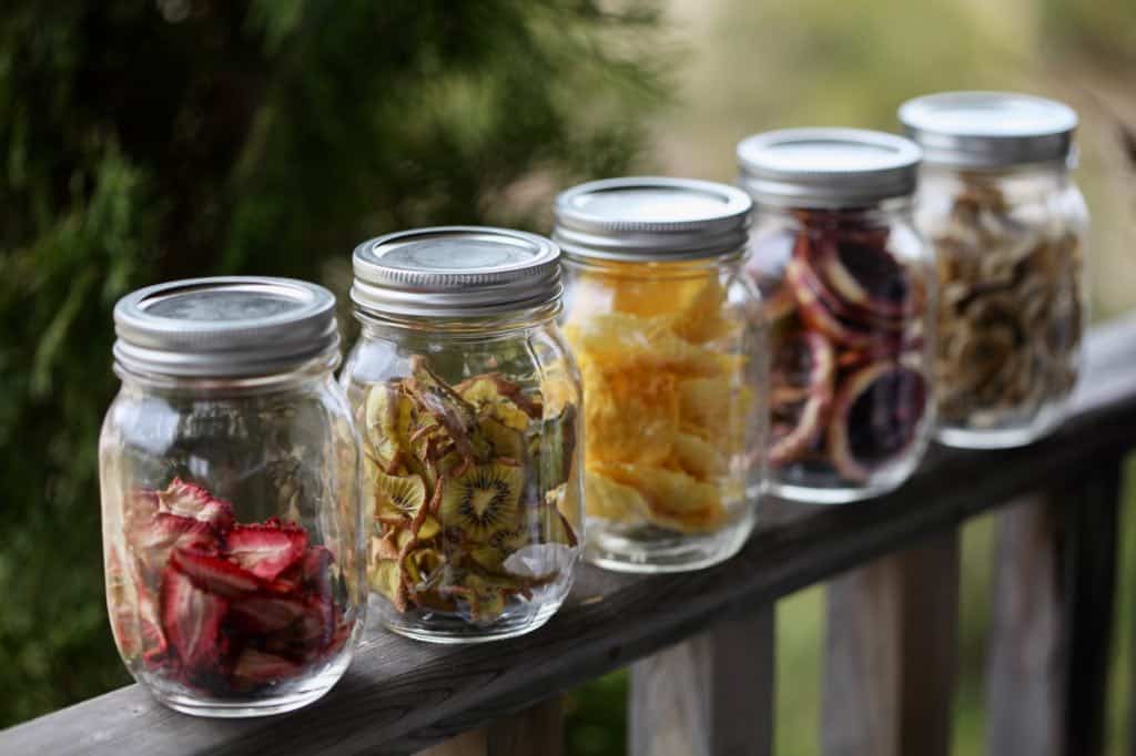 dehydrated fruit in mason jars on a wooden railing