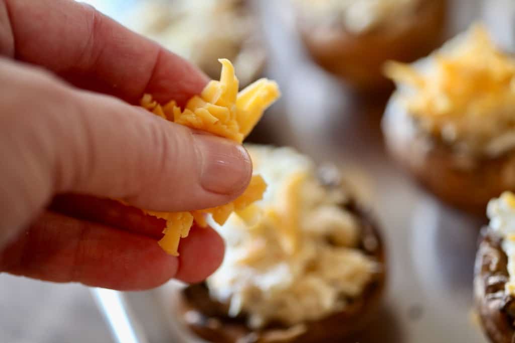 a hand topping mushroom caps with cheddar cheese