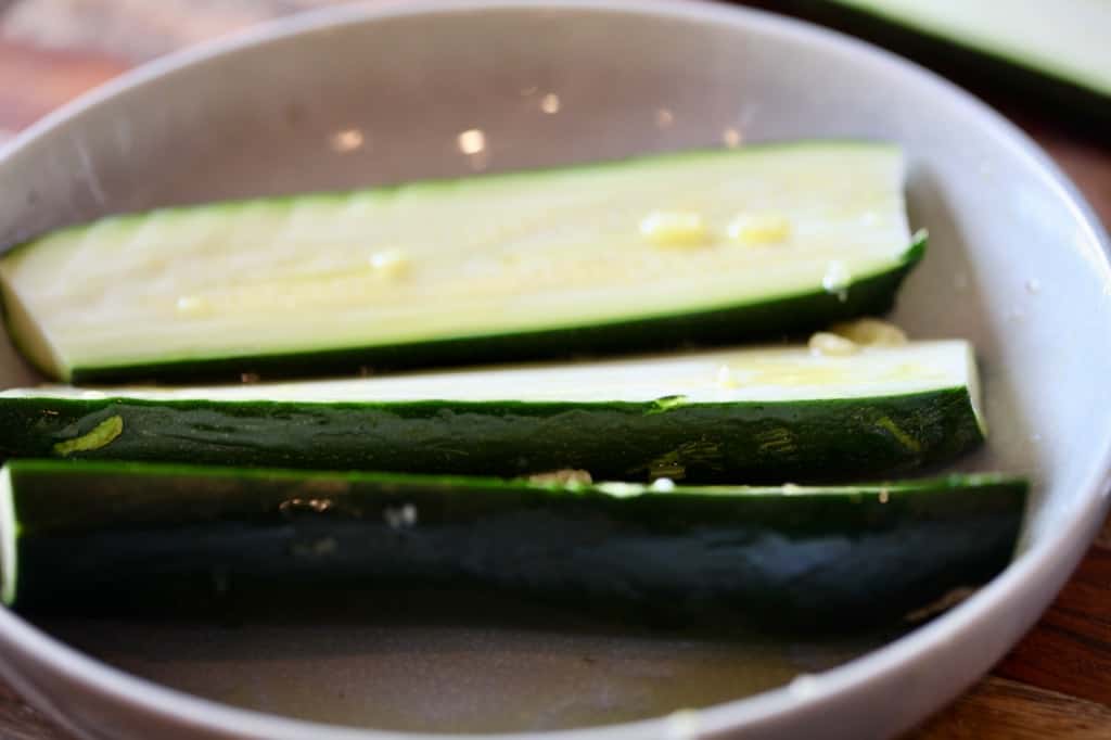 coating the cut zucchini pieces with oil in a white bowl