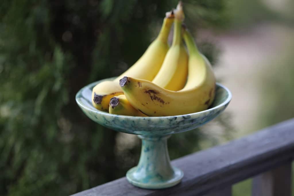 a bunch of bananas on a green platter, on a wooden railing