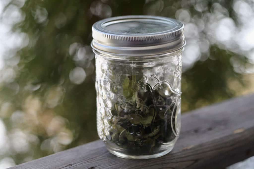 a mason jar full of dried mint on a wooden railing