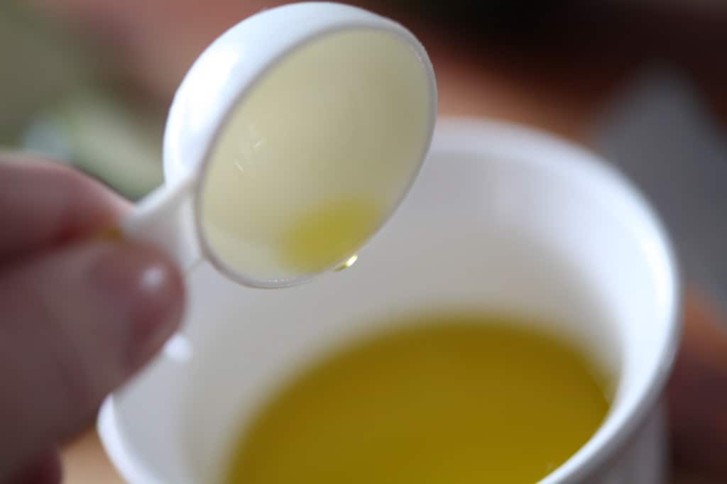 measuring out the olive oil into a white bowl with a measuring spoon