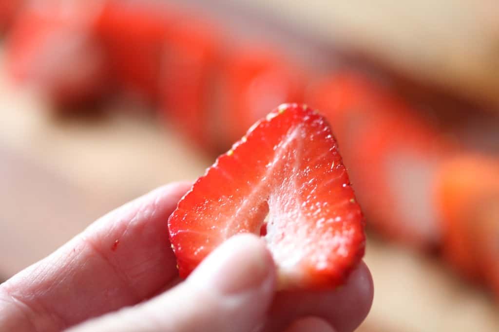 a hand holding a sliced strawberry piece