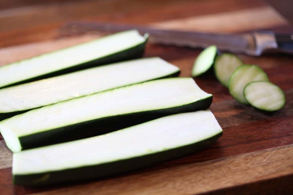 zucchinis cut into halves on a wooden cutting board next to a knife