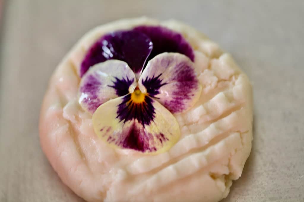 a pansy flower covered with egg white to secure in place on a cookie