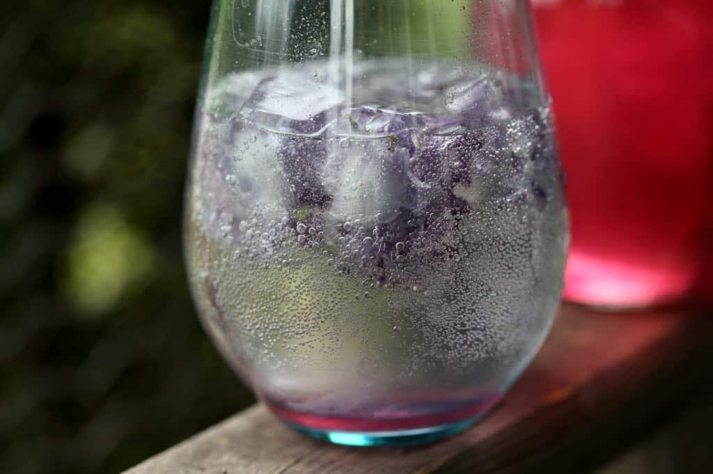 a glass of carbonated water with lilac infused syrup and lilac ice cubes