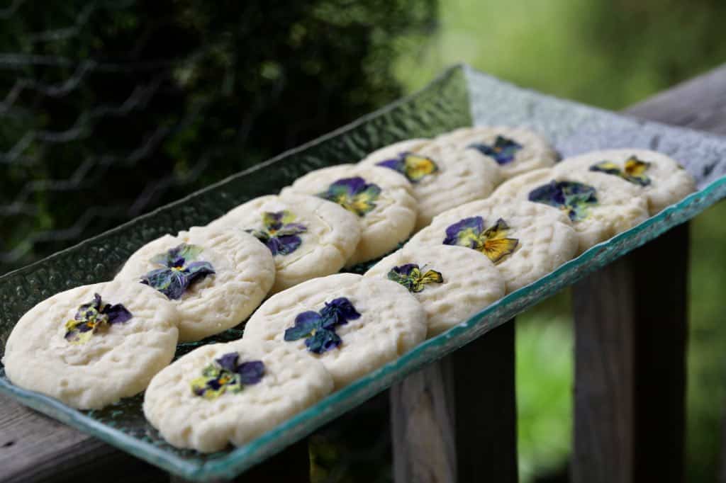 shortbread decorated with pansies and violas, on a glass tray on a wooden railing