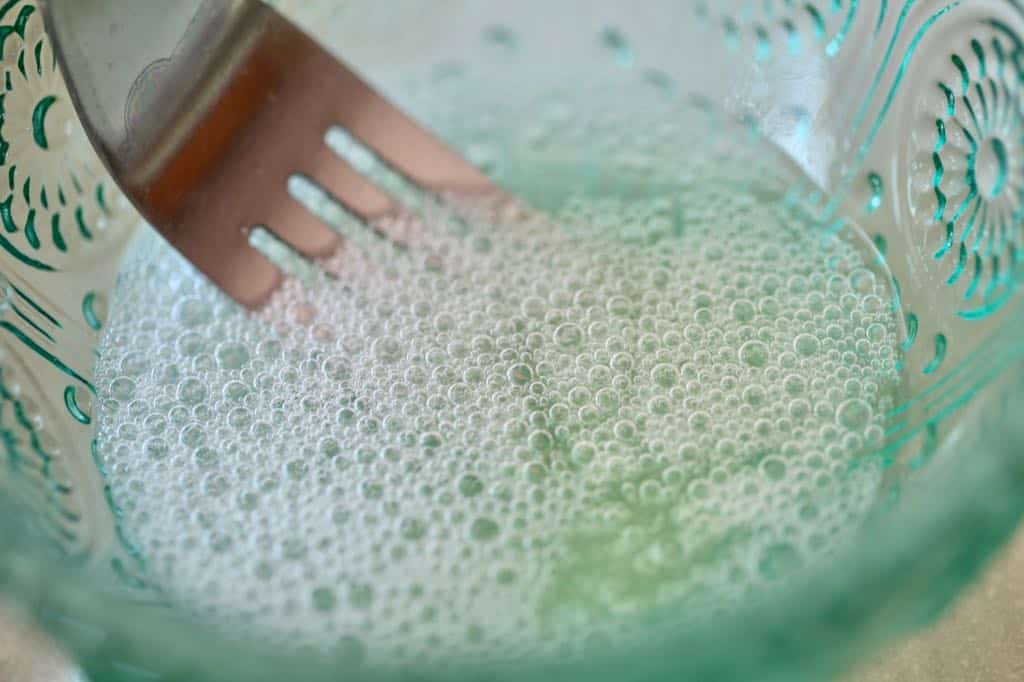 a fork whisking egg white and water in a green bowl until frothy