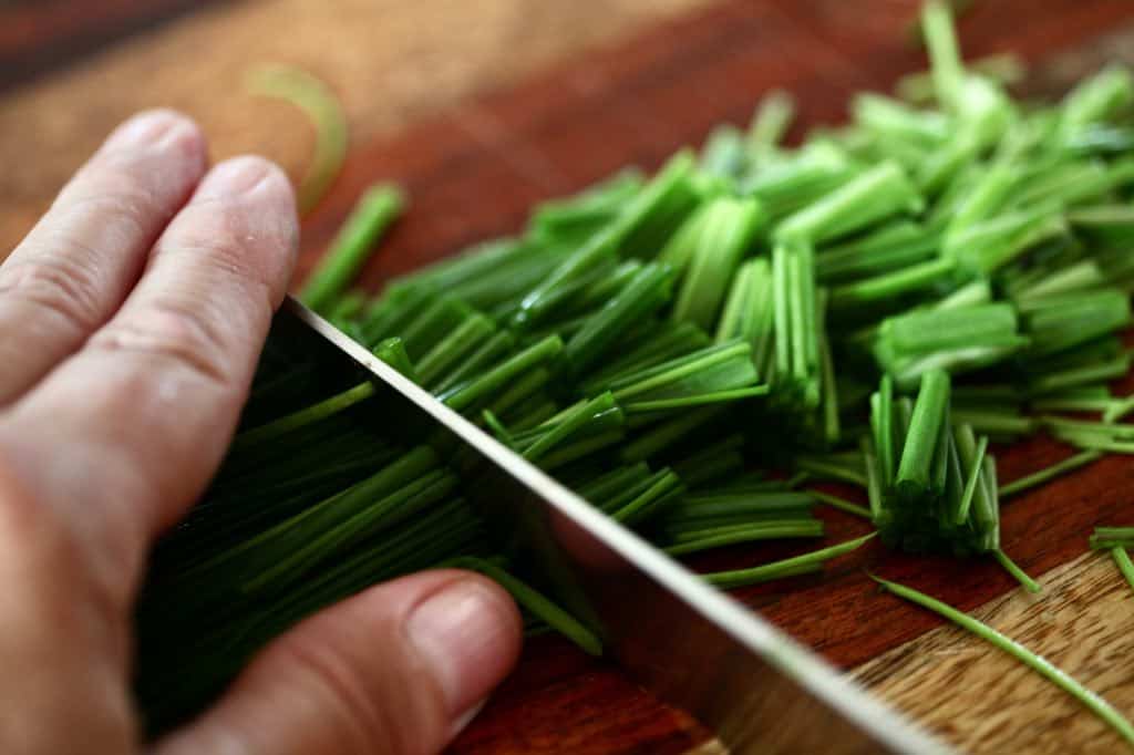 a hand chopping chives into small pieces