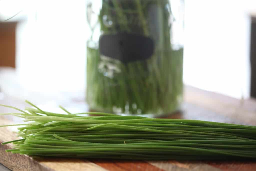 chives on a cutting board next to a glass container of water with chives