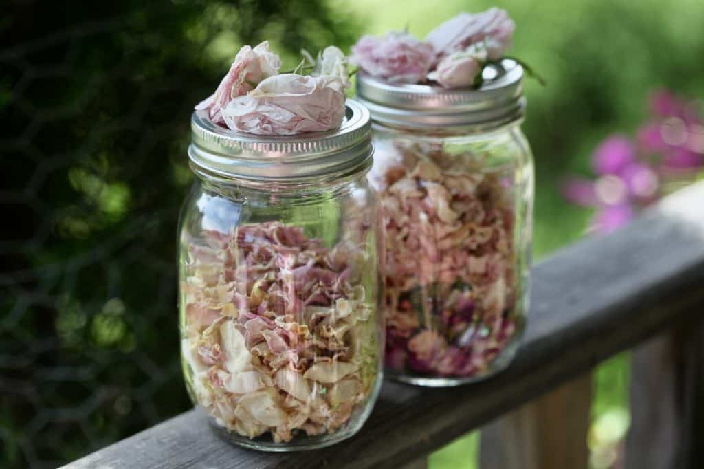 dried rose petals in glass mason jars on a wooden railing