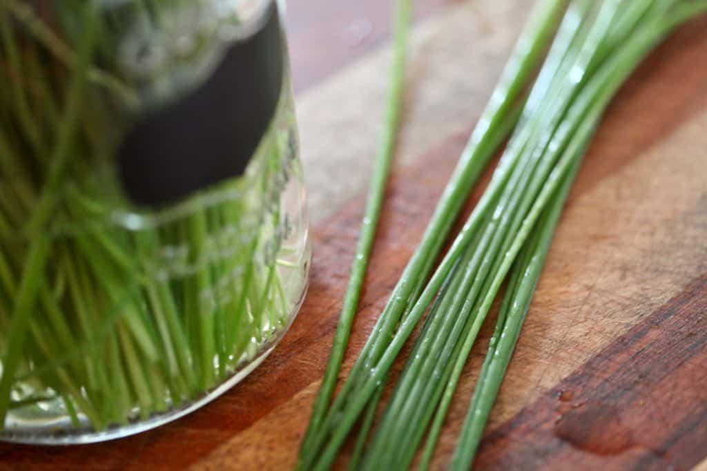 wet chives on a wooden cutting board next to a glass container with water and chives